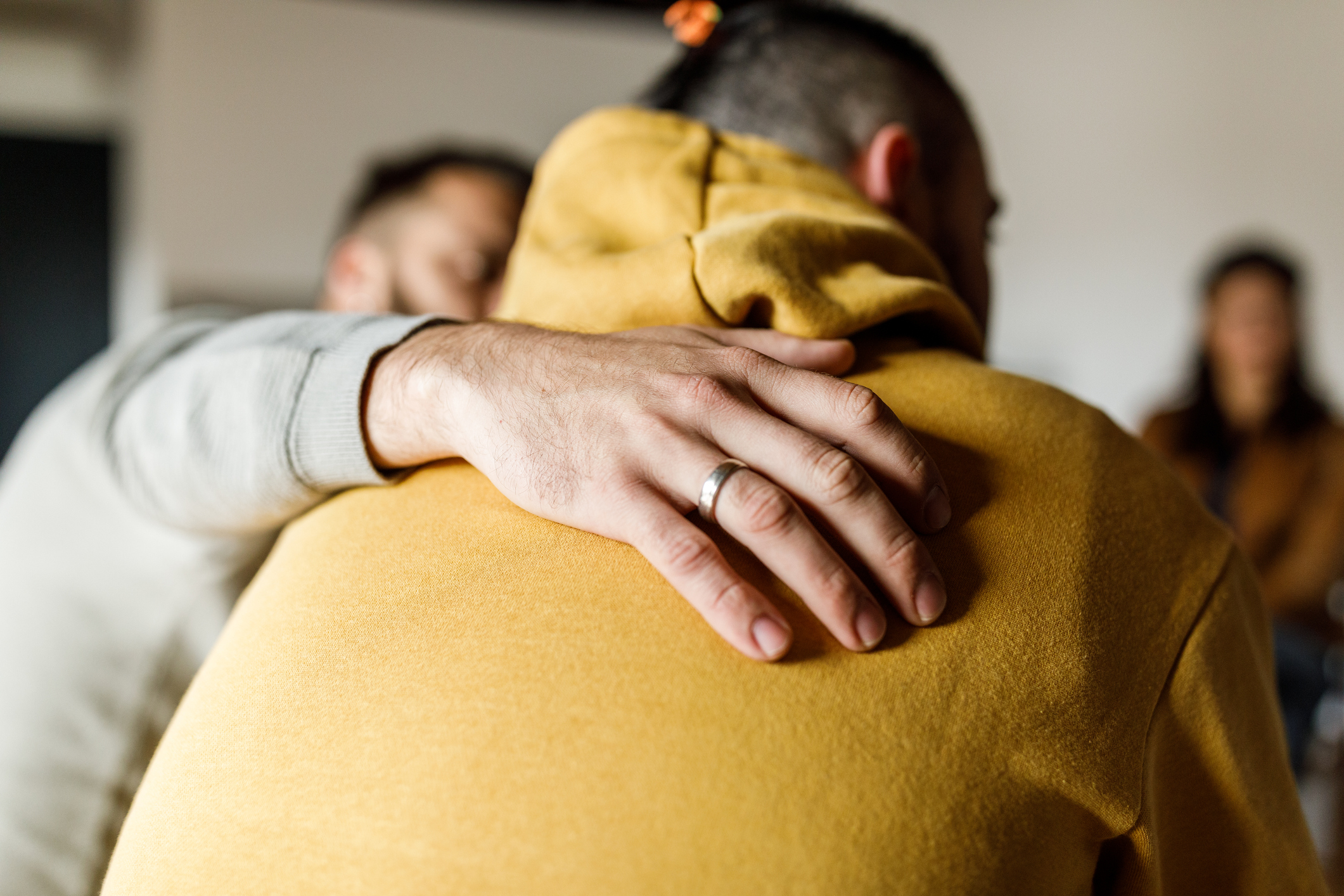 Le dos d’un homme avec un pull jaune. Une autre main est placée sur le dos pour signaler les soins.