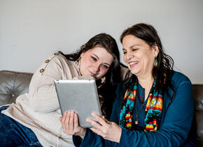 Deux femmes souriantes en regardant une tablette.